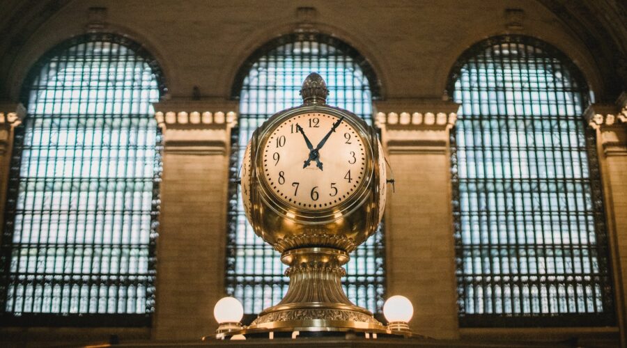 vintage golden clock in aged railway station terminal with arched windows