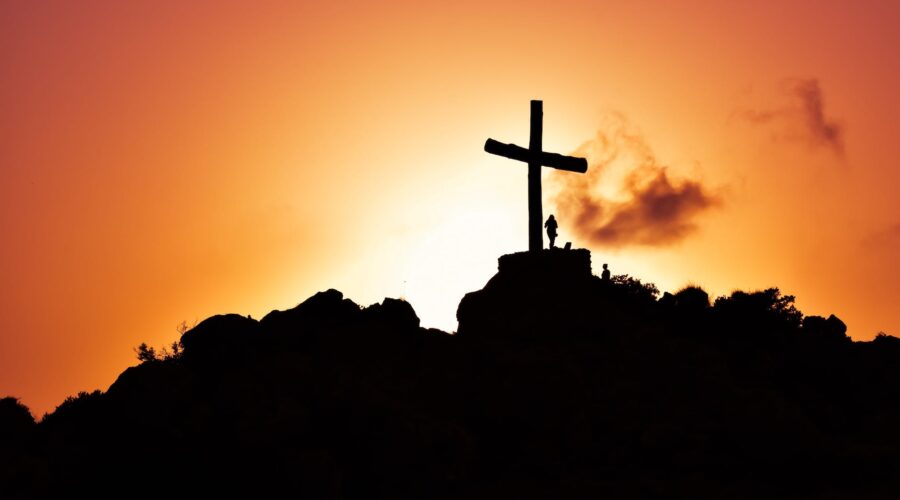 human standing beside crucifix statue on mountain