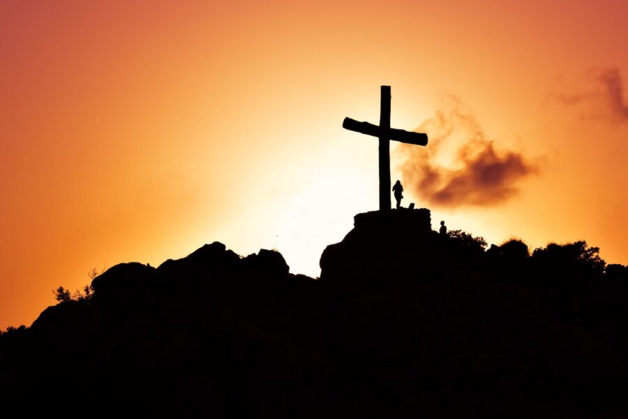 human standing beside crucifix statue on mountain