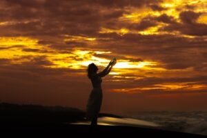 silhouette of a woman standing on the beach with her arms raised at sunset